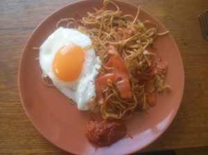 Fried noodles on a plate, with a fried egg and chili paste